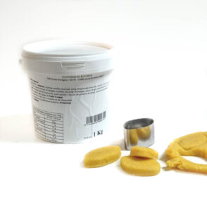 White plastic tub with a printed label next to a small metallic cookie cutter and several yellow round cookies on a white surface.