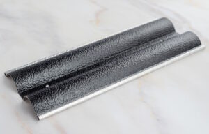 Two black textured metal trims with silver glitter edging lying on a marble surface.