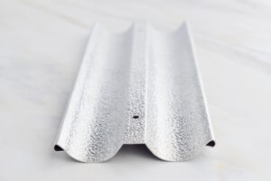 Close-up of a galvanized steel channel rail with a central hole on a light surface.
