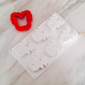 Red flower-shaped cookie cutter beside a white tree-shaped cookie mold on a pale marble countertop.