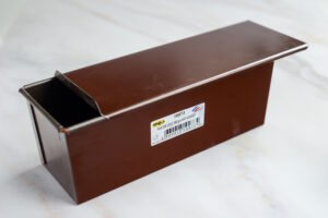 Brown metal rectangular box with a partially open top, placed on a light marble surface.