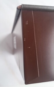 Close-up of a brown leather or faux-leather case edge with a black protective strip at the top, showing small scratches along the side.