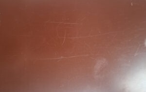 Close-up of a brown scratched table surface with numerous light, white scratches and scuffs across it.