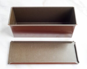 Two empty brown rectangular baking pans, one upright and one flat on a white surface on a marble-like background.