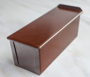 Brown rectangular metal case with a hinged lid, viewed at an angle on a light surface